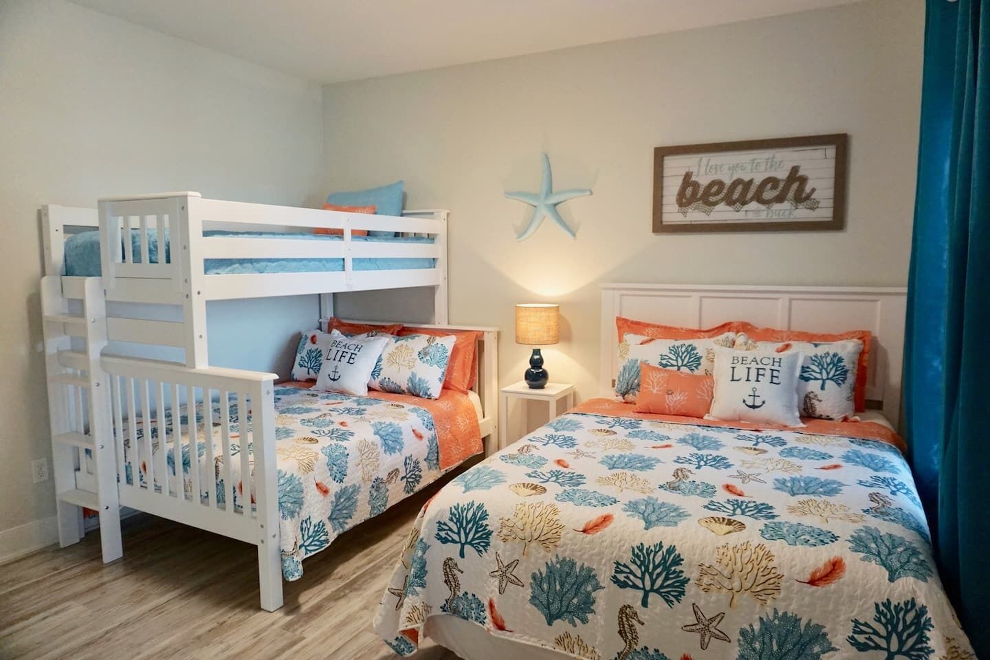 Camera da letto con due letti, uno a castello e l'altro standard. Entrambi i letti sono rifiniti con cuscini decorativi coordinati e una coperta a tema spiaggia.