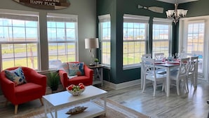Un salon spacieux avec vue sur la plage, un coin repas avec des meubles blancs et un ventilateur de plafond.