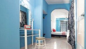 Una habitación con paredes azules, una cama con cabecera blanca, un taburete pequeño y un espejo con marco decorativo.