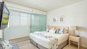 A bedroom with a bed, bedside tables, a TV, and a window with blinds. - Unit 101 Plantation Resort - Rainbow Beach. Plantation Resort. Second Floor. Aircon. Pool. Spa.Wifi (Rainbow Beach)
