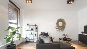 A modern living room with a sectional sofa, a round coffee table, a decorative wall hanging, and a built-in shelving unit. - Sack-Time 6: Luxury & relaxation near the sea! (Zandvoort)