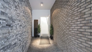 A narrow hallway with brick walls and a tiled floor, leading to a door at the end. - Sack-Time 6: Luxury & relaxation near the sea! (Zandvoort)