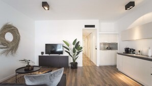 A modern living room with a sofa, a TV, a small table, and a potted plant. There is a kitchen area with cabinets and a countertop. - Sack-Time 6: Luxury & relaxation near the sea! (Zandvoort)