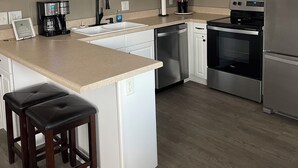 A modern kitchen with white cabinets, stainless steel appliances, a central island with stools, and a sign reading "BEACH". - Ocean Lakes  Clean Home for your Family! Now booking for 2026. (Myrtle Beach)