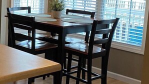 A dining area with a wooden table and chairs, a hanging light fixture, and large windows with a city view. - Ocean Lakes  Clean Home for your Family! Now booking for 2026. (Myrtle Beach)