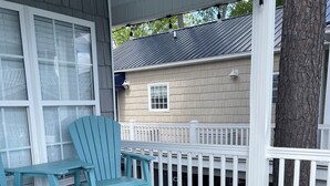A covered porch with turquoise chairs and a small table, a white railing, and a tree trunk. - Ocean Lakes  Clean Home for your Family! Now booking for 2026. (Myrtle Beach)