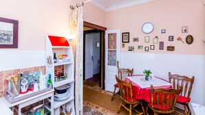 Un comedor con una mesa dispuesta para dos, sillas de madera, mantel rojo, y una pared con cuadros y un reloj.