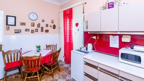 Cocina compacta con comedor, que incluye un reloj, varios electrodomésticos y una cortina roja.