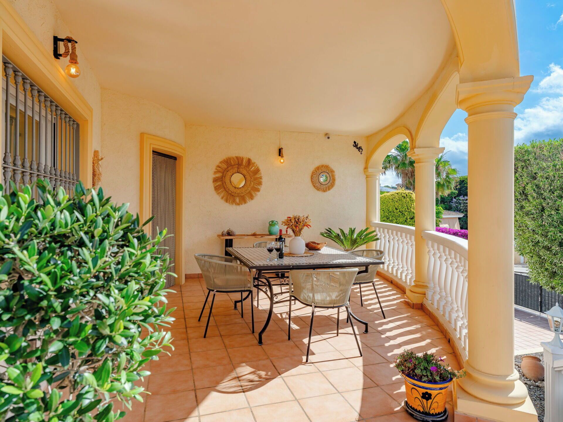 Un patio cubierto con una mesa y sillas, un espejo decorativo y vistas al jardín.