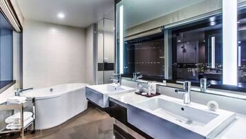 A modern bathroom with two sinks, a large bathtub, and a mirror reflecting a cityscape.