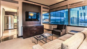 A modern living room with a flat-screen TV, dark wood cabinets, a sofa, and a coffee table. - City Center! | Panoramic Corner Suite at Vdara (Las Vegas)
