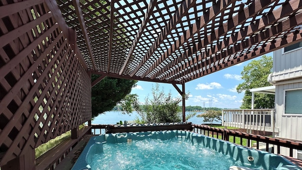 Un jacuzzi bajo una pérgola de madera con vista a un lago.