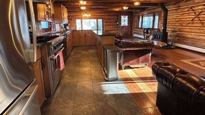 Cocina de cabaña de madera con armarios de madera, un refrigerador de acero inoxidable, una isla central y una chimenea.