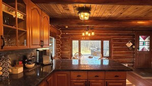 Cocina rústica con armarios de madera, encimera de granito y comedor con vistas al exterior.