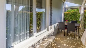 A covered patio with a table and chairs, large windows with curtains, and a stone accent wall. - Lovely apartment in villa for 6 guests with pool, WIFI, A/C, TV, terrace and pets allowed (Banjole)