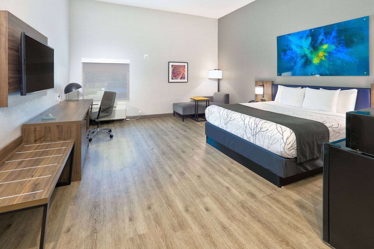 A modern hotel room with a wooden desk, a comfortable bed, a flat-screen TV, and a large abstract painting on the wall.