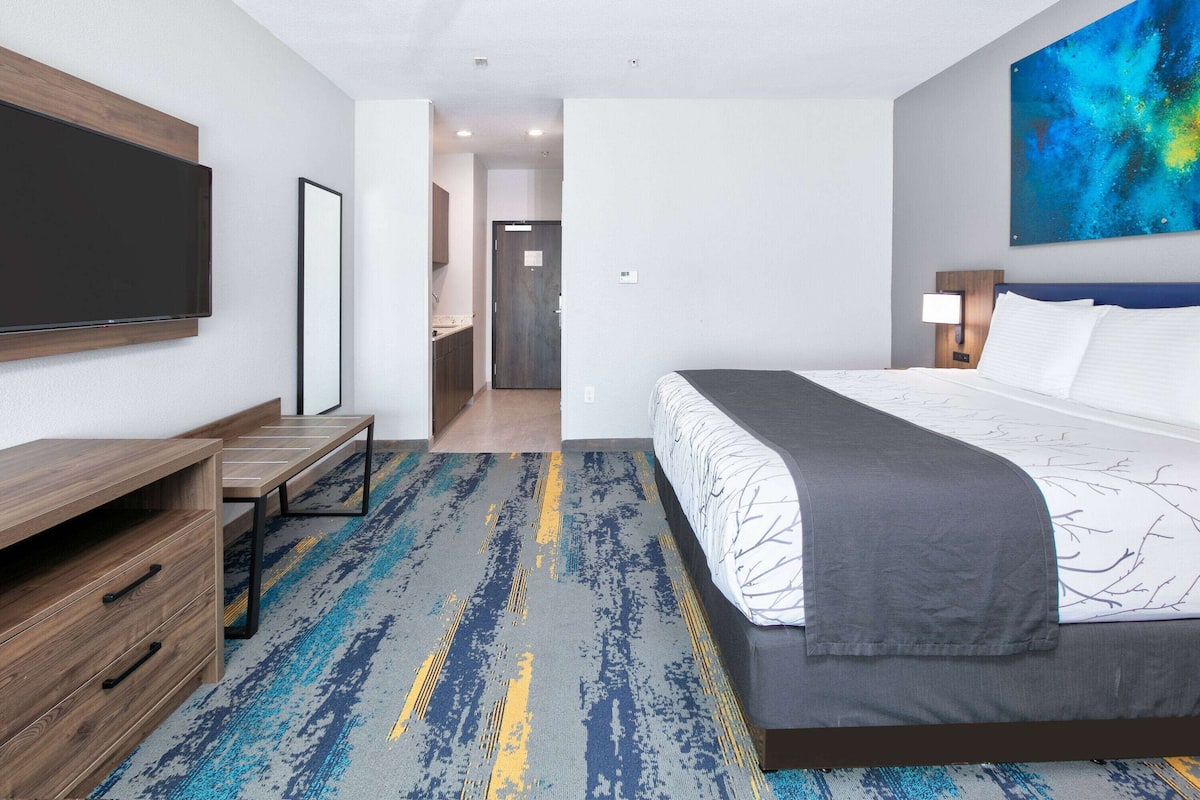 A hotel room with a bed, a desk, a TV, and a painting on the wall.