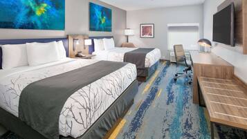 A hotel room with two beds, a desk, a chair, a TV, and artwork on the walls.