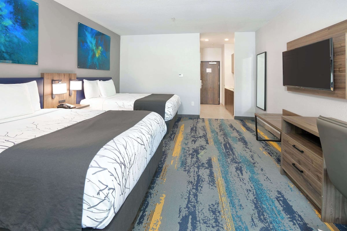 A hotel room with two beds, a TV, a desk, and a bathroom visible through an open door.