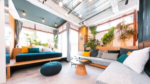Una sala de estar moderna con sofá, reposapiés y mesa de centro. Hay plantas en macetas y un ventanal que proporciona luz natural.