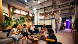 Un grupo de personas sentadas alrededor de una mesa con comida y bebidas en una sala moderna, bien iluminada, con plantas y una escalera.