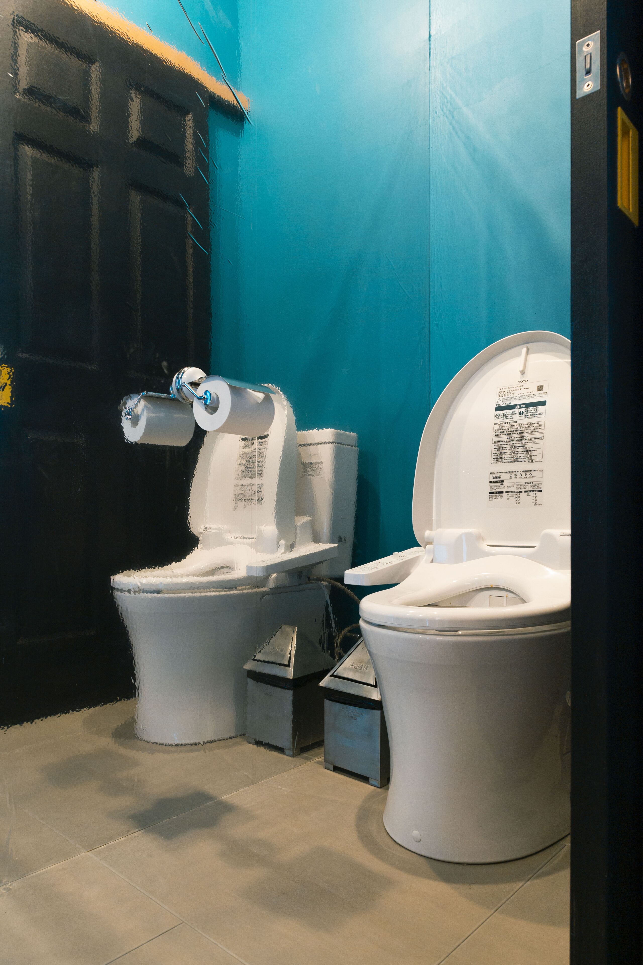 Two toilets in a bathroom with a blue wall and a black door.