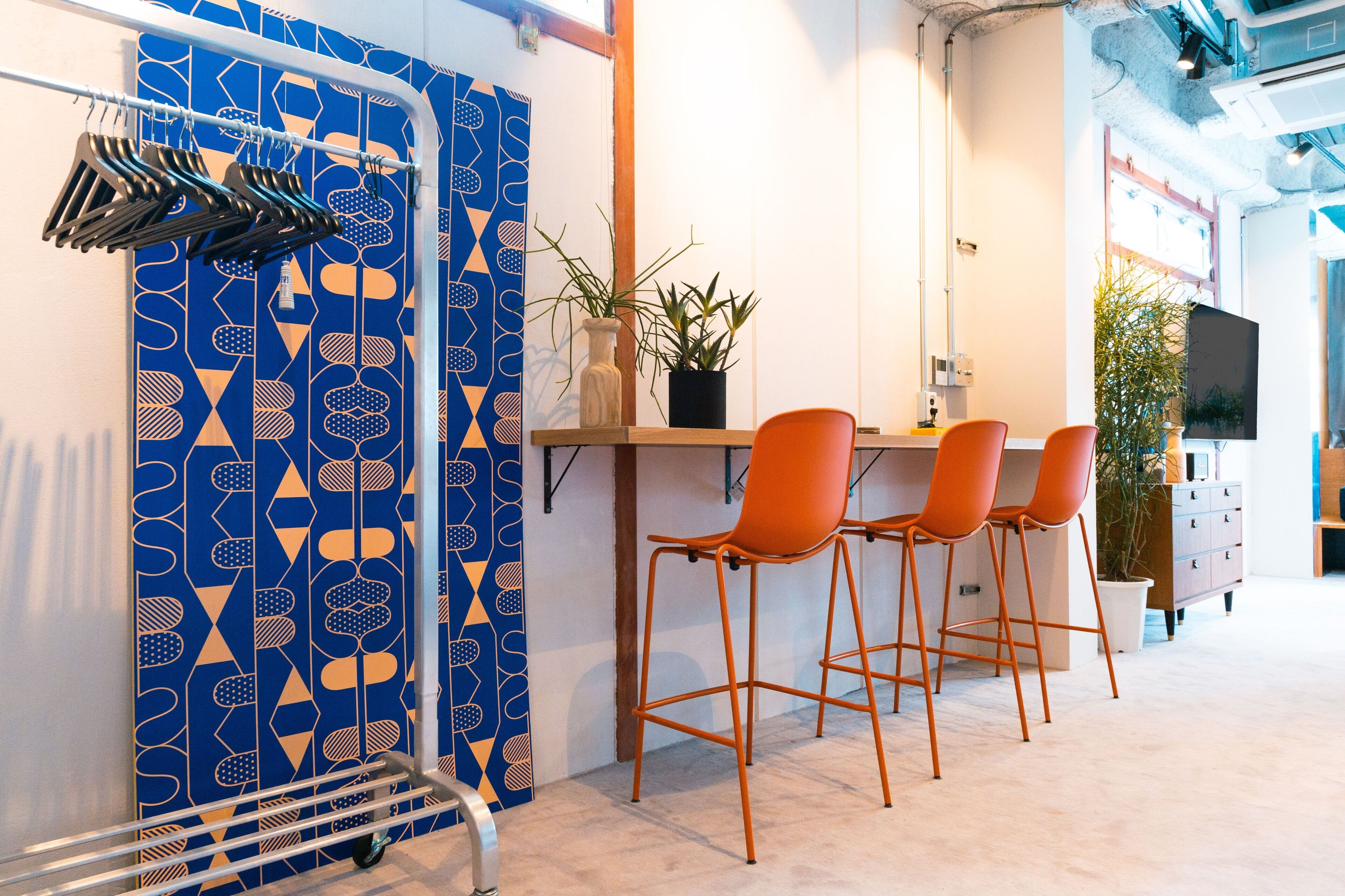 A modern bar area with a geometric patterned wall, a wooden counter, orange bar stools, and a potted plant.