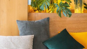 Una habitación con cabecera de madera, cama con almohadas a rayas y de colores lisos, lámpara colgante y varias plantas verdes.