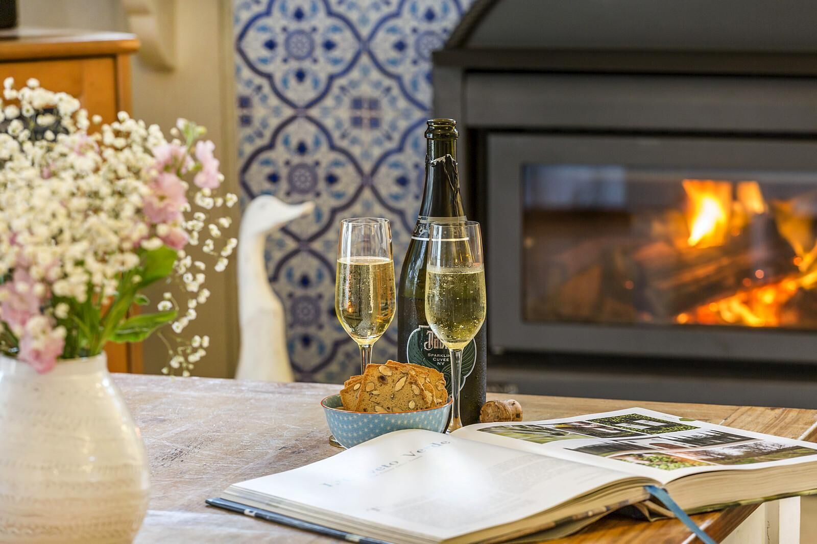 Une table avec deux verres de vin blanc, une bouteille de vin mousseux, un bol de noix et un livre.