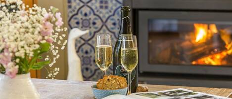 Une table avec deux verres de vin blanc, une bouteille de vin mousseux, un bol de noix et un livre.