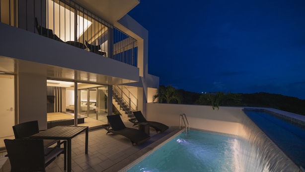 Ett modernt hus med en swimmingpool, utomhusmöbler och en trappa som leder upp till en balkong.