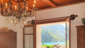 A room with a chandelier, a table with a bottle and a vase, and a view of a lake and mountains through an open door.