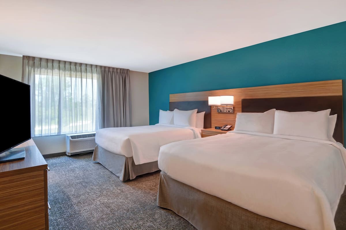 A hotel room with two beds, a TV, a desk, and a window with curtains.
