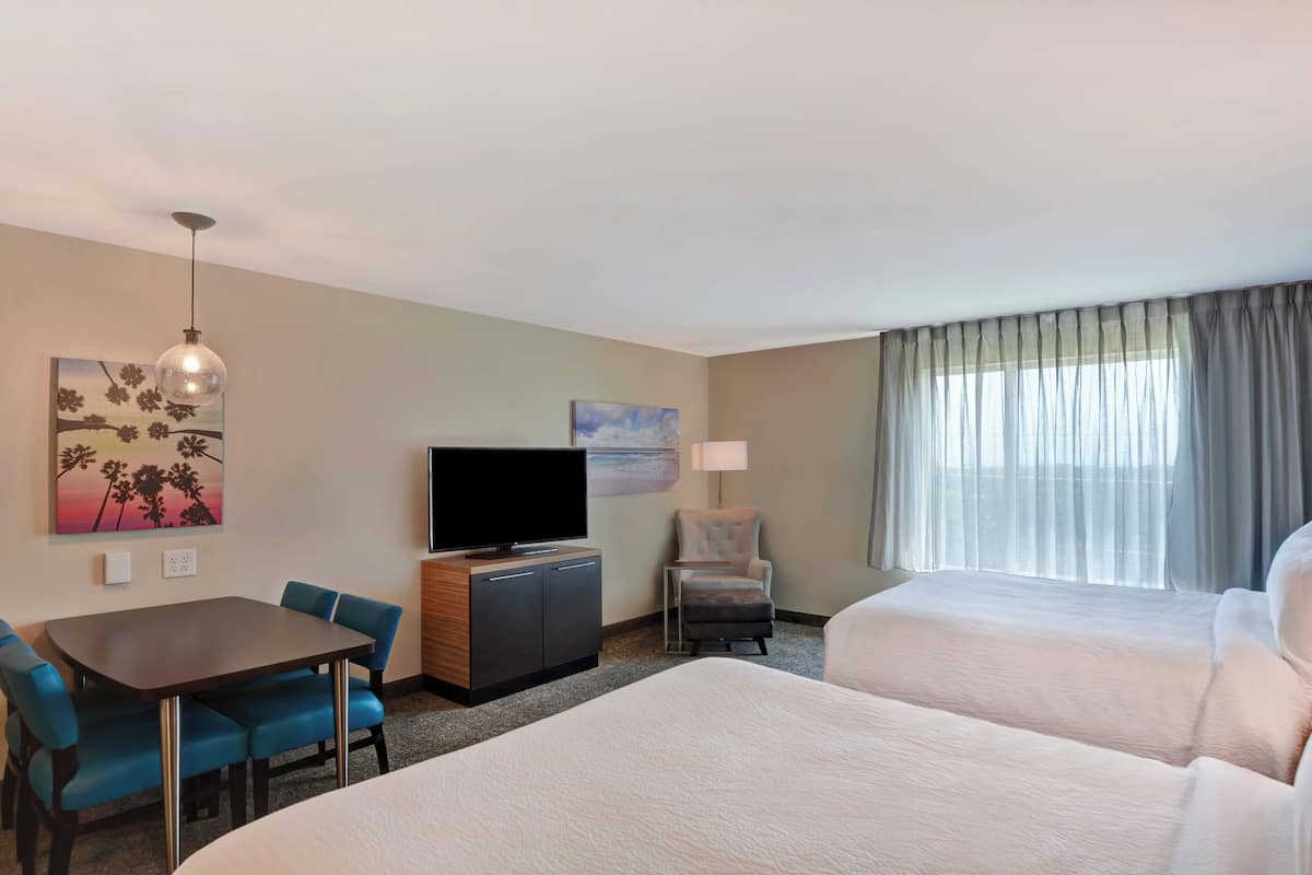 A hotel room with a bed, a desk with a chair, a television, a lamp, and a window with curtains.