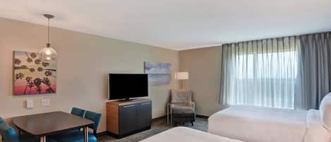A hotel room with a bed, a desk with a chair, a television, a lamp, and a window with curtains.