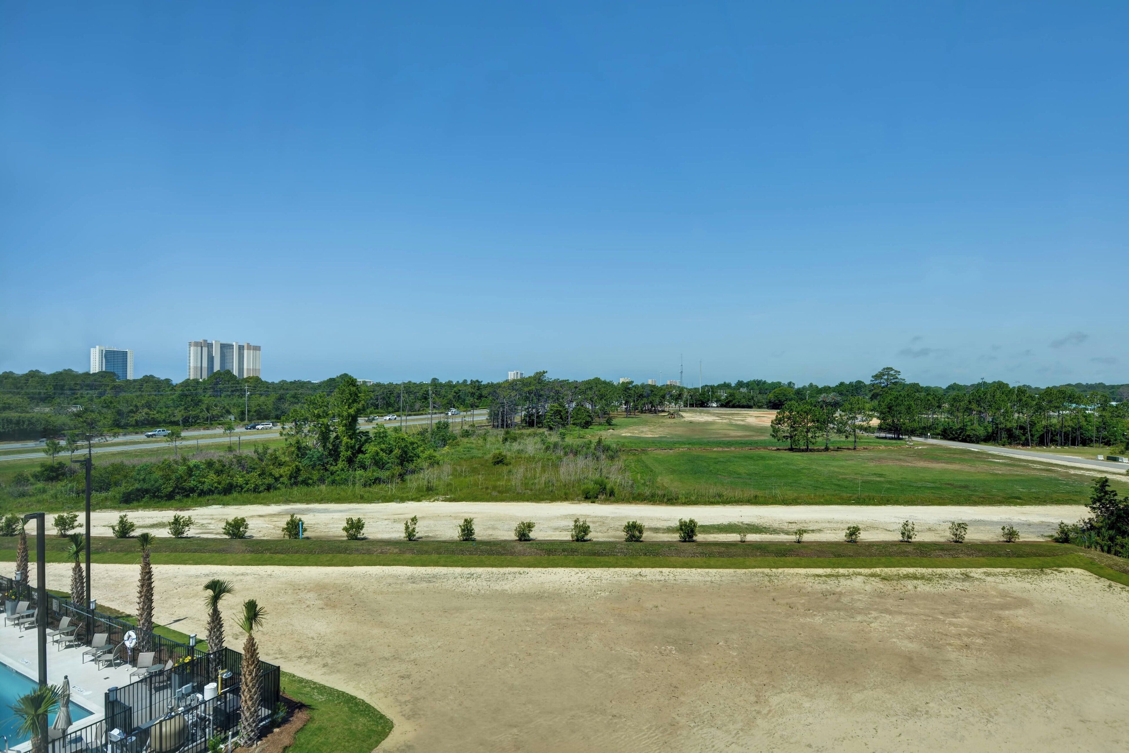 A hotel with a pool area, outdoor seating, and a view of a golf course and distant buildings.