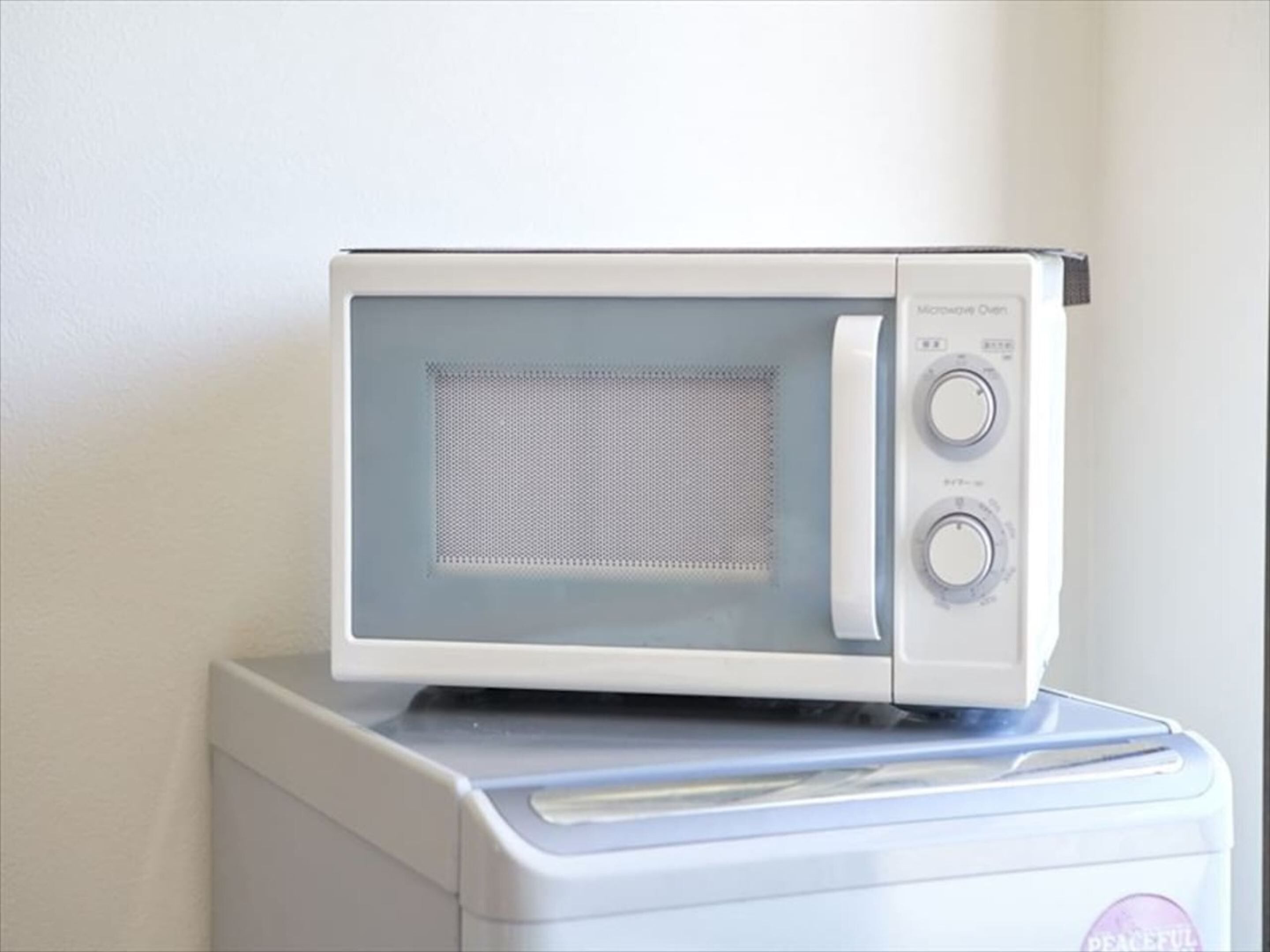 A microwave oven placed on top of a washing machine.