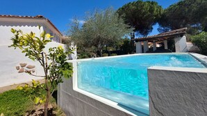 Une piscine bordée de pierres, entourée de verdure et adossée à un bâtiment blanc doté d’un toit en tuiles.