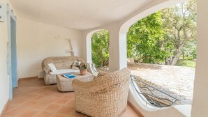 Un espace extérieur aménagé, abrité et doté de mobilier en osier, avec vue sur un jardin.