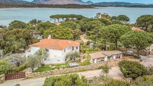 Une propriété située sur la côte, avec un bâtiment blanc, un mur en pierre et une vue sur la mer et les montagnes.