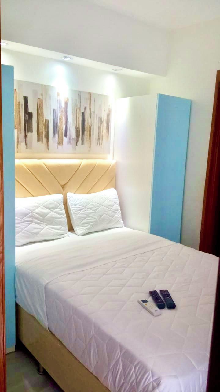 Ein ordentlich bezogenes Bett mit einer gesteppten weißen Decke, zwei Kissen und einem Kopfteil mit geometrischem Muster.