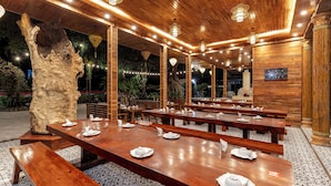 Een restaurant met houten tafels en banken, een grote boomsculptuur en een klok aan de muur.