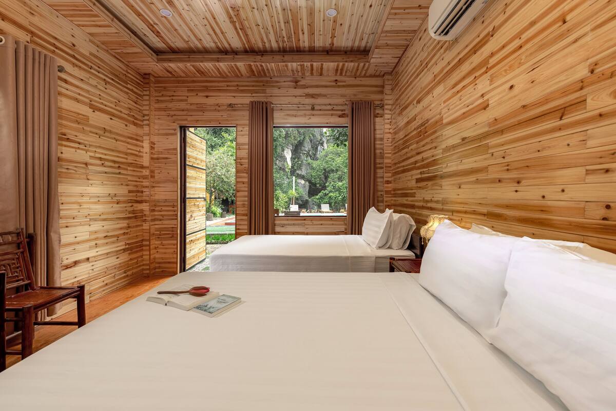 A wooden-paneled room with a large bed, a chair, and a window offering a view of greenery.
