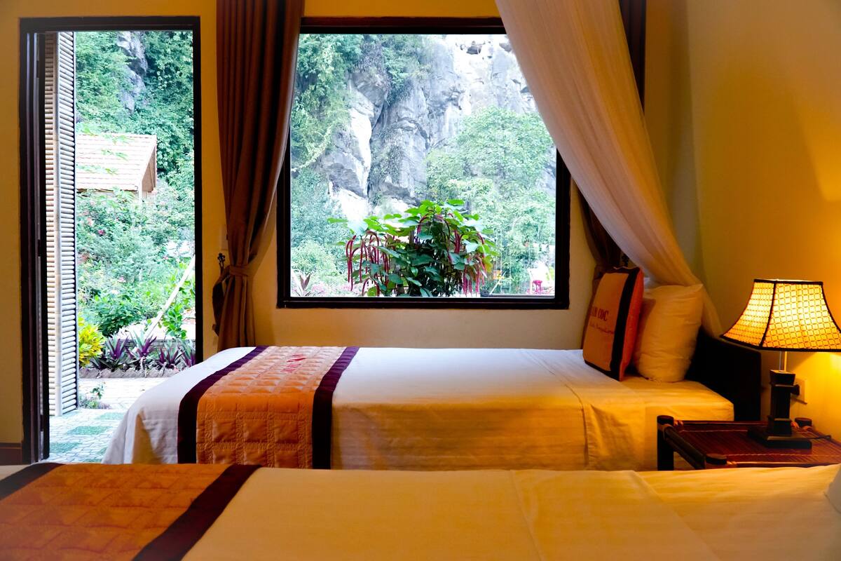 A hotel room with a bed, a nightstand, a lamp, and a window with curtains.