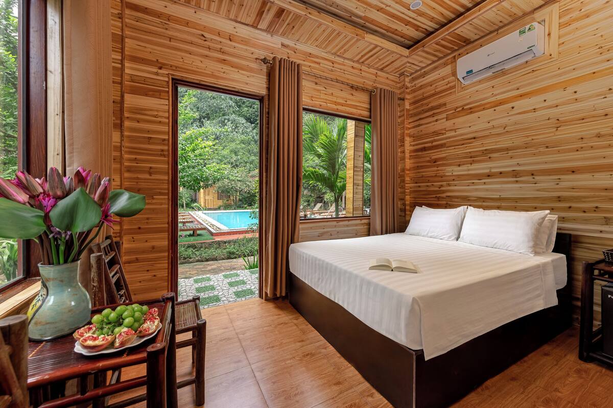 A wooden-paneled room with a bed, a dining table with a plate of food, and a view of a swimming pool.
