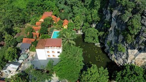 Luchtbeeld van een resort met een zwembad, omgeven door weelderige begroeiing en een rotsachtige klif.