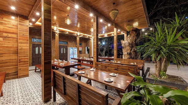 Een restaurant met houten inrichting, tafels, banken en een grote boom ervoor.