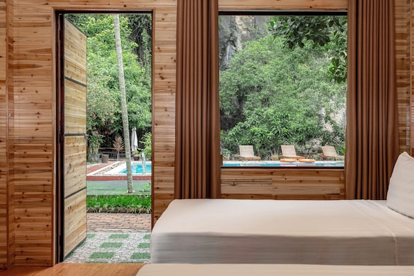 Una habitación de madera con una cama, vista a una piscina y un paisaje verde exuberante.