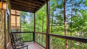 Une terrasse en bois avec des chaises, un mur en pierre et une vue sur une forêt.
