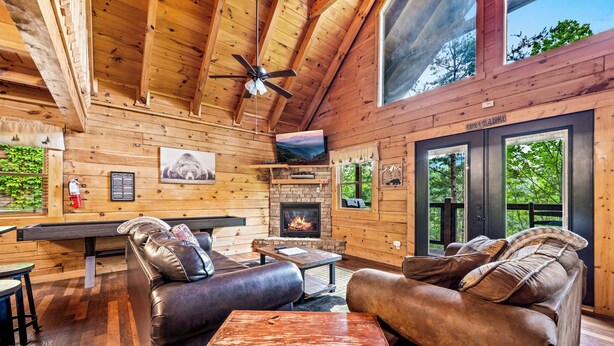 Un intérieur de chalet chaleureux avec des murs en bois, une cheminée, des canapés en cuir et un téléviseur.
